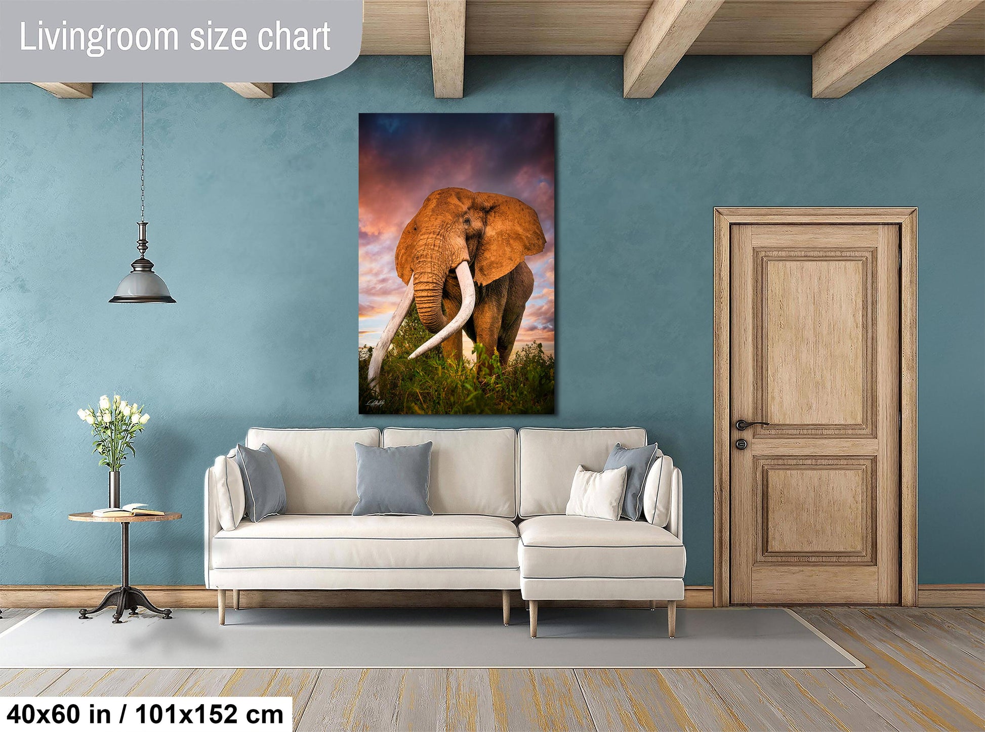 a living room with a large elephant painting hanging on the wall. The elephant is standing in a grassy field with trees in the background, creating a serene and natural atmosphere. The living room is furnished with a white sofa and a wooden door, providing a cozy and inviting space.