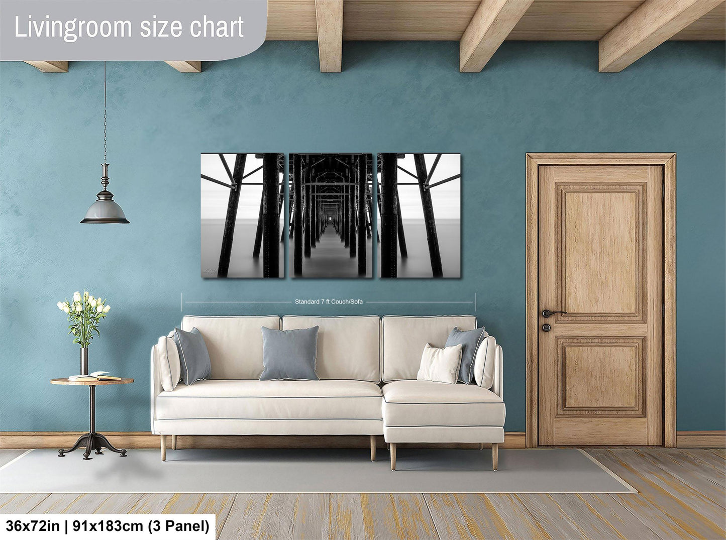 The image is a living room with a large white sofa, a wooden door, and a wall with a large black and white photograph of a bridge. The room has a blue wall and a wooden floor.