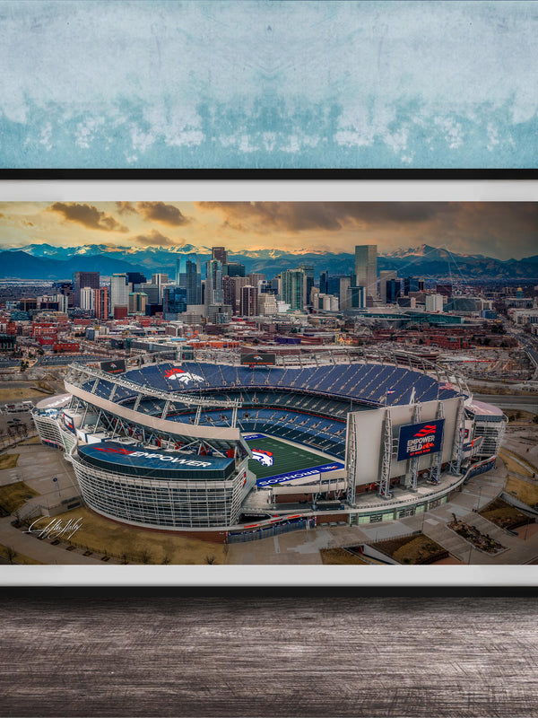 The image is an aerial view of a large sports stadium, likely a football stadium, with the city skyline in the background.
