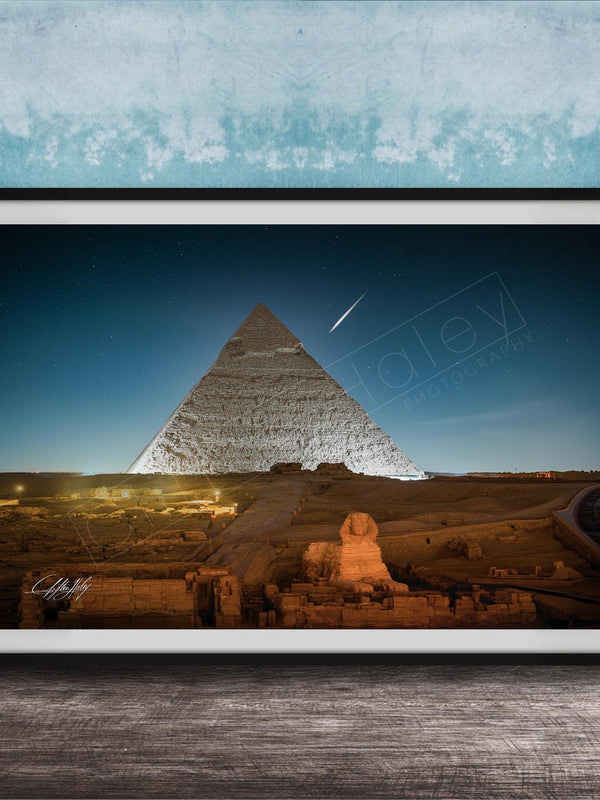 A framed photograph of the Great Pyramid of Giza at night, with the pyramid illuminated against a dark blue sky.