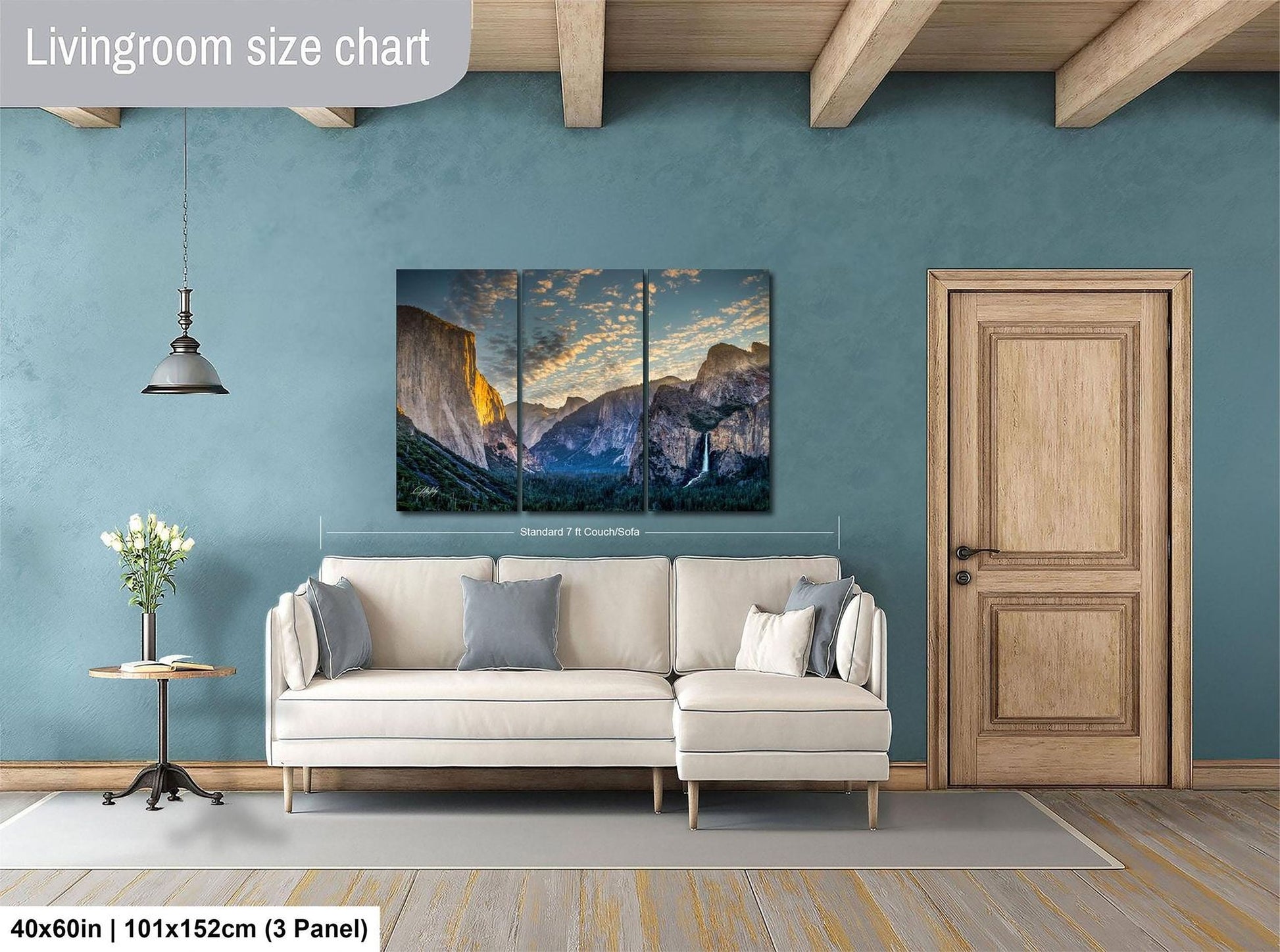 The image is a living room with a large, three-panel landscape painting hanging on the wall. The painting depicts a scenic mountain range with a sunset in the background. The room has a white sofa and a wooden door, creating a cozy and inviting atmosphere.