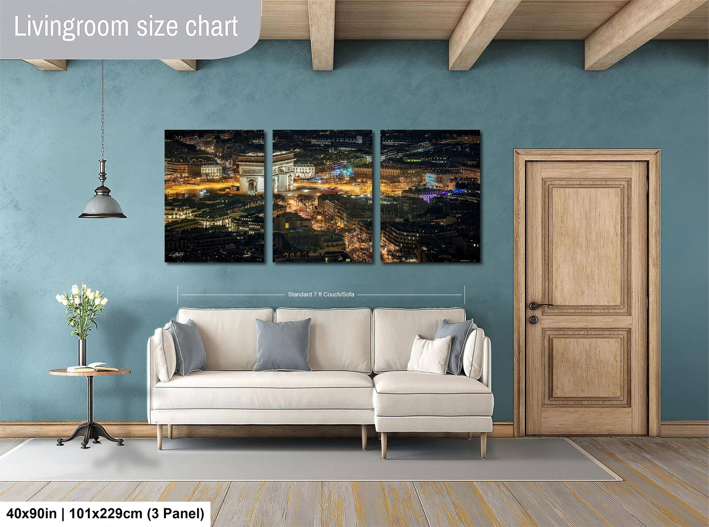 The image is a living room with a large, three-panel, high-resolution cityscape painting hanging on the wall. The painting depicts a nighttime cityscape with illuminated buildings and lights. The room is furnished with a white sofa and a wooden door, and there is a potted plant and a vase on a side table. The painting is approximately 40 inches wide and 101.29 cm tall, with a 3-panel layout.