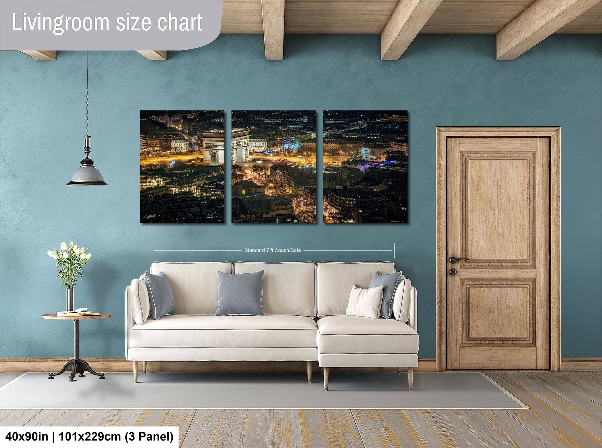 The image is a living room with a large, three-panel, high-resolution cityscape painting hanging on the wall. The painting depicts a nighttime cityscape with illuminated buildings and lights. The room is furnished with a white sofa and a wooden door, and there is a potted plant and a vase on a side table. The painting is approximately 40 inches wide and 101.29 cm tall, with a 3-panel layout.