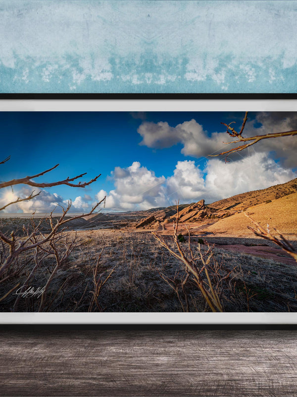 A framed photograph depicting a desert landscape with a blue sky, clouds, and a dry, barren terrain.