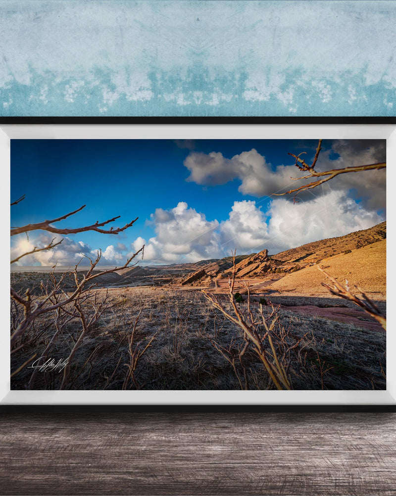 A framed photograph depicting a desert landscape with a blue sky, clouds, and a dry, barren terrain.