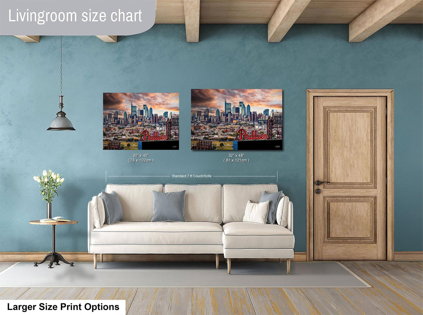 a living room with a white sofa and a wooden door. Above the sofa, there are two framed pictures of a city skyline, with the word "Phillies" written on them. The living room has a blue wall and a wooden ceiling.