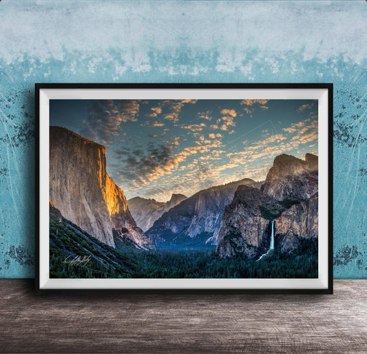 The image is a framed photograph of a breathtaking mountainous landscape, with towering cliffs, a waterfall, and a vibrant sky filled with clouds.