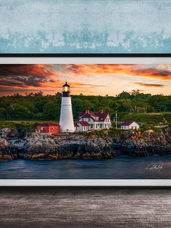 A framed photograph of a lighthouse on a rocky shore, with a colorful sunset sky in the background.